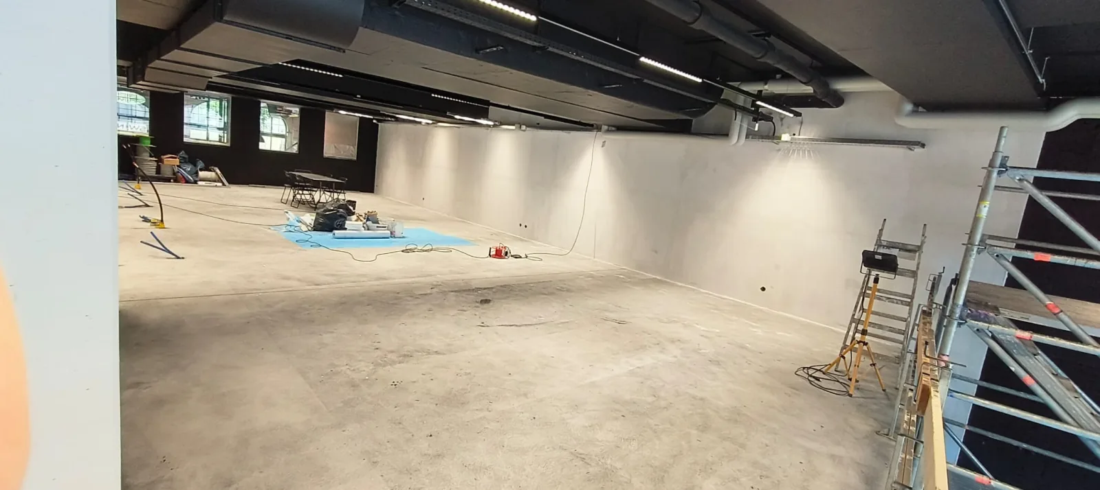 Wide view of a large open hall with freshly plastered walls and ductwork running across the ceiling