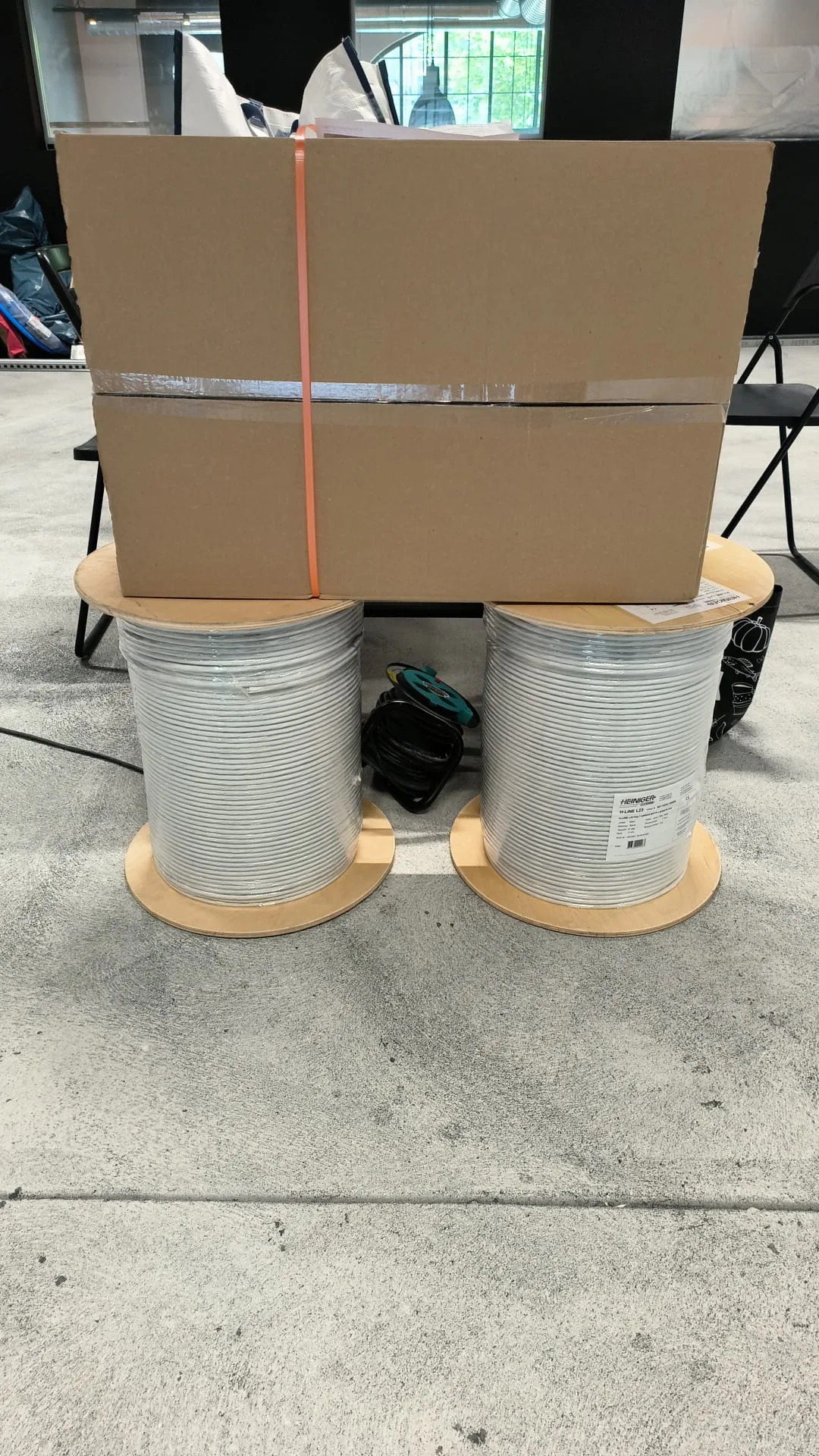 Two large spools of cable next to a taped cardboard box on the concrete floor