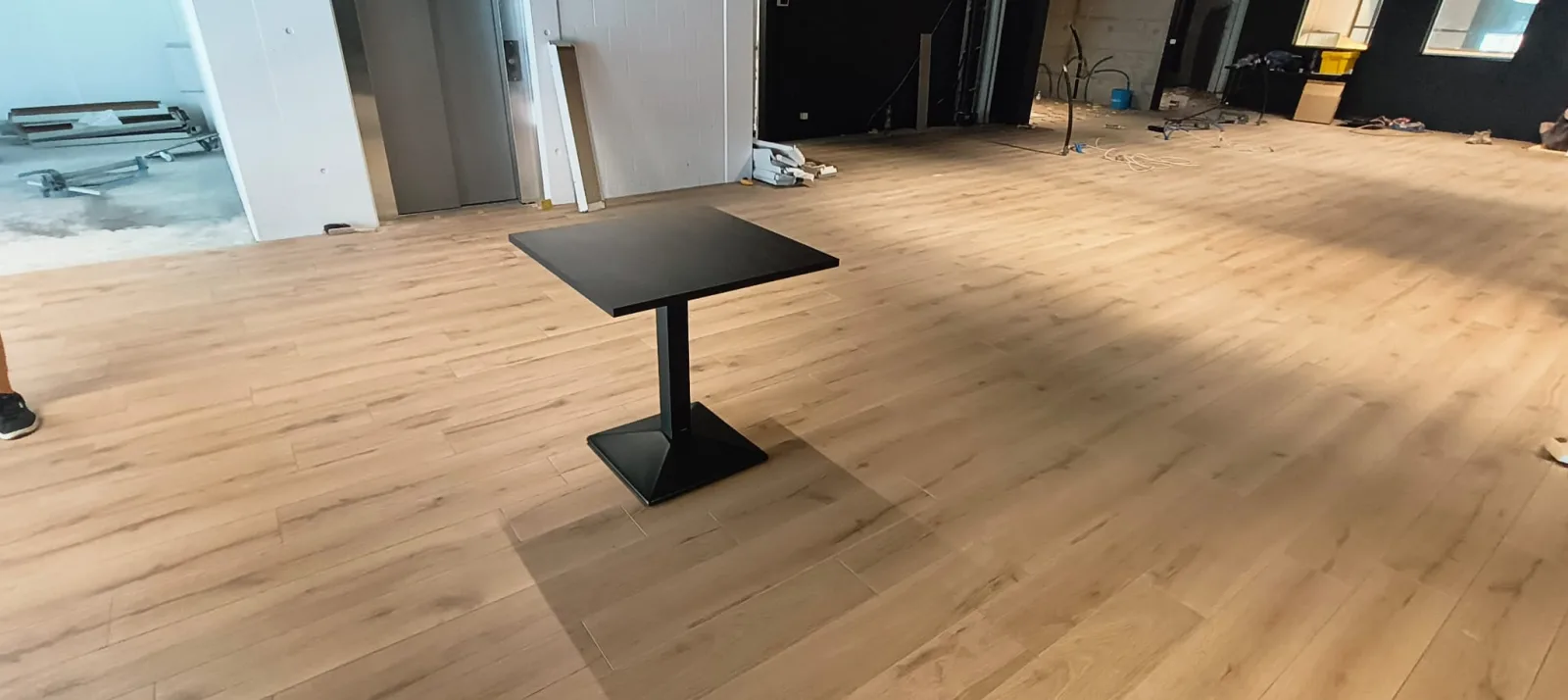 The finished oak wood floor stretching across the open hall with a single black bistro table in the middle