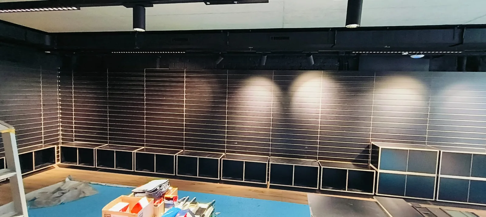 Black slatwall wall fitted with cube shelving and warm spotlights above the new wood floor
