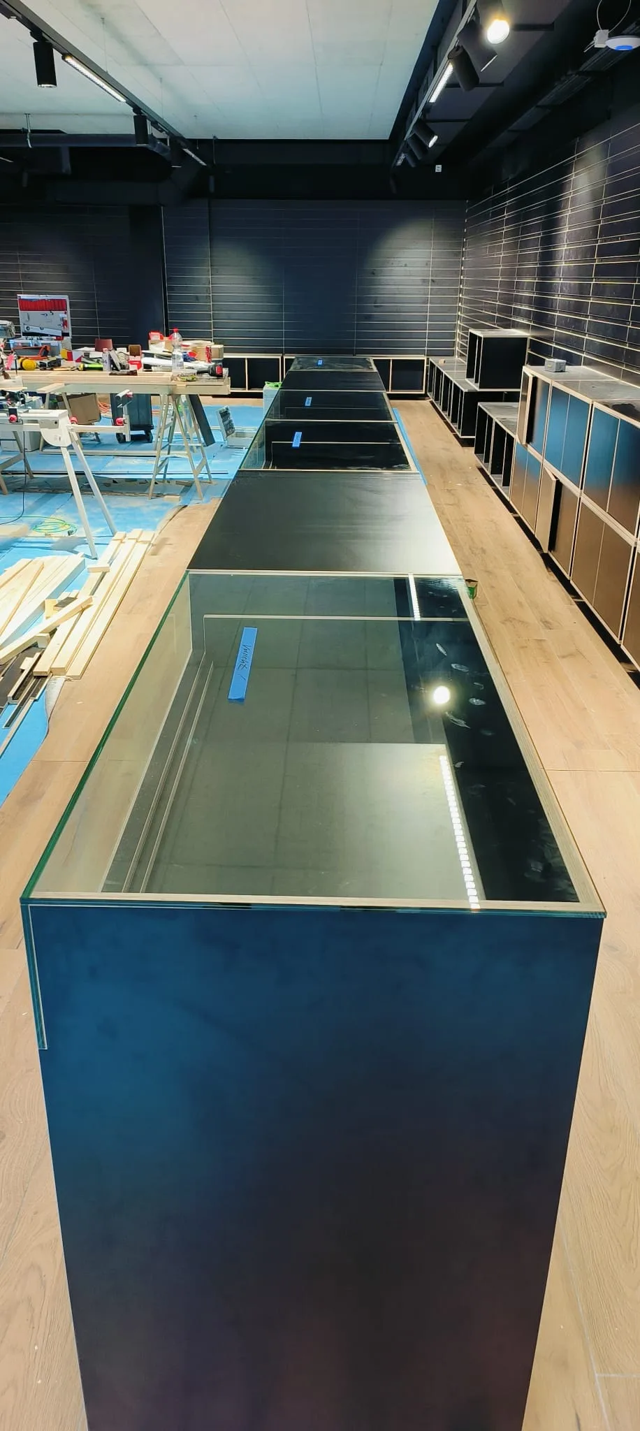 Long glass display counter down the middle of the shop, with a workshop bench and timber to the side