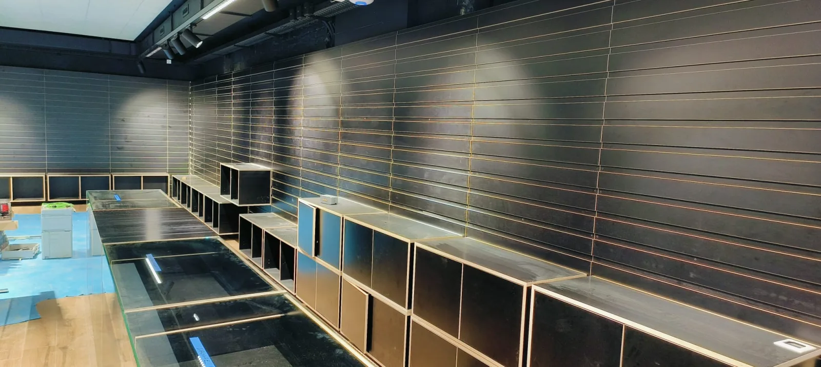 Black slatwall retail shelving with wooden-edged cabinets and a glass display counter running along the shop
