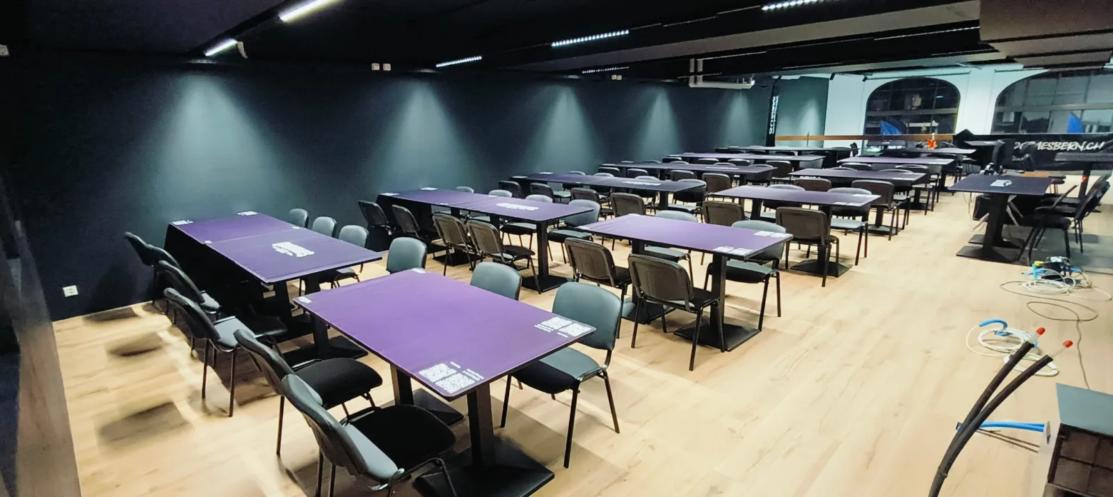 Wide view of the finished tournament hall with purple GoodGames Bern tables and chairs in front of the arched windows