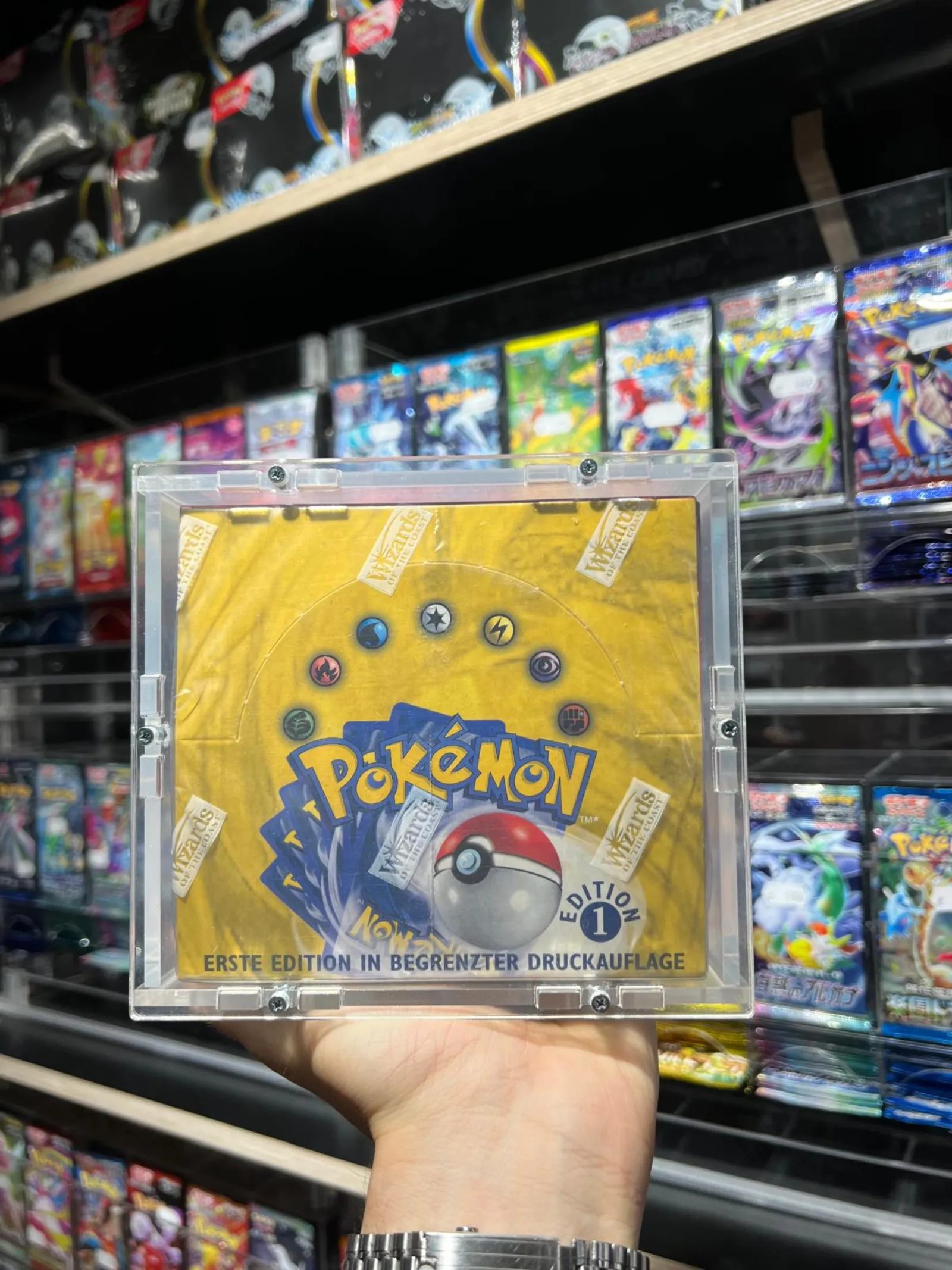 A sealed first-edition Pokémon base set booster box held up in front of the shelves