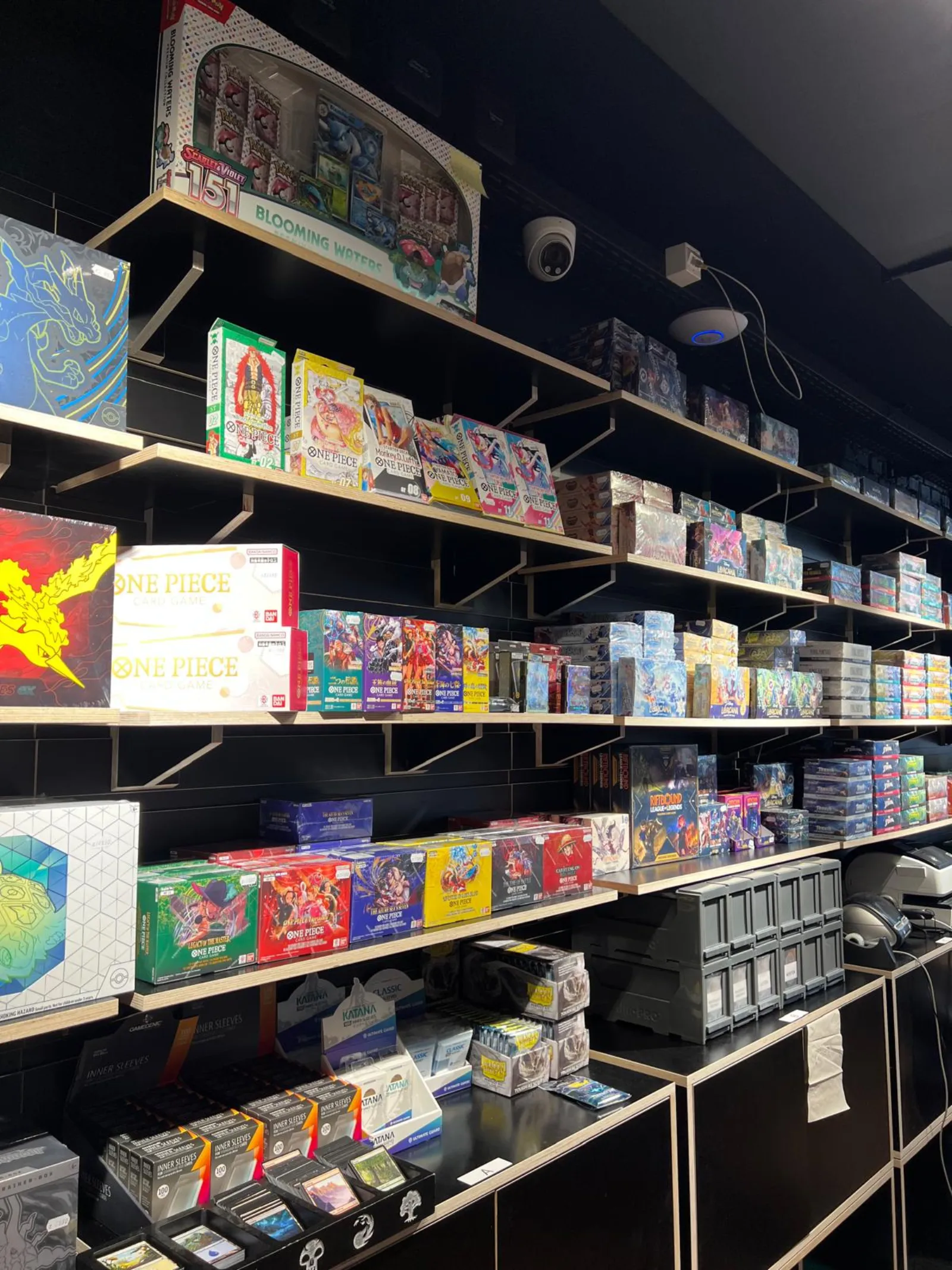 Shelves stacked with One Piece and Pokémon booster boxes and display cases
