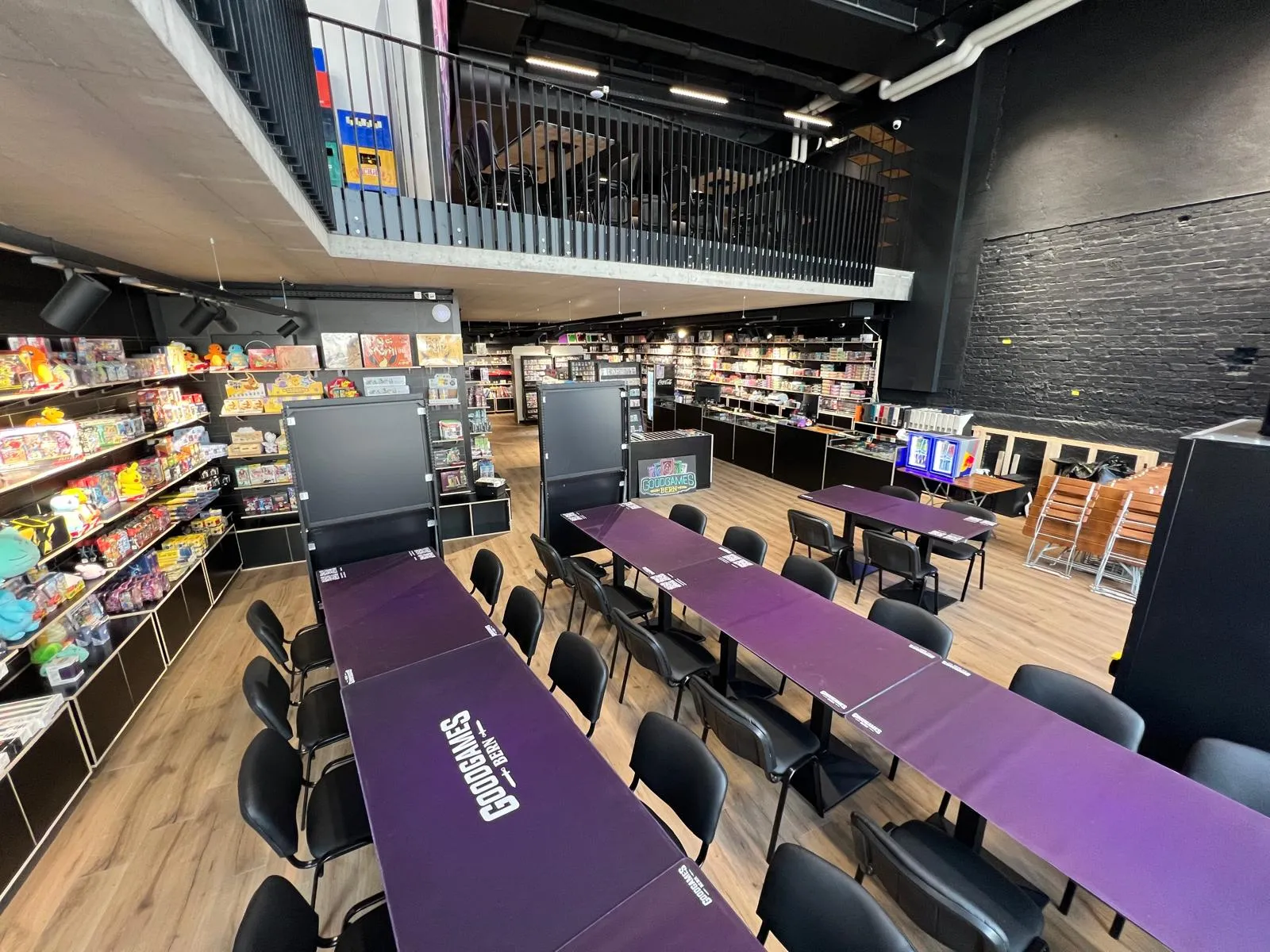 The play area seen from above, purple GoodGames Bern tables lined up next to the card shelves
