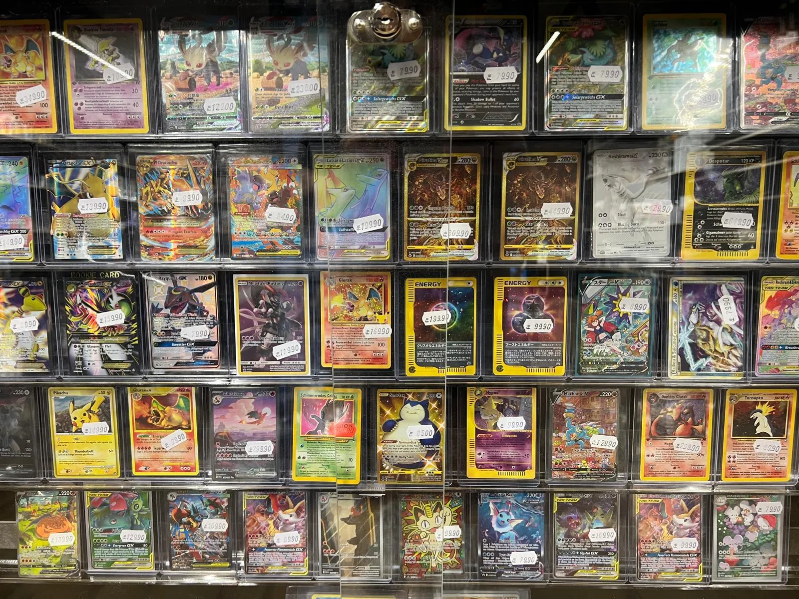 A wall of single Pokémon cards in sleeves with handwritten price tags