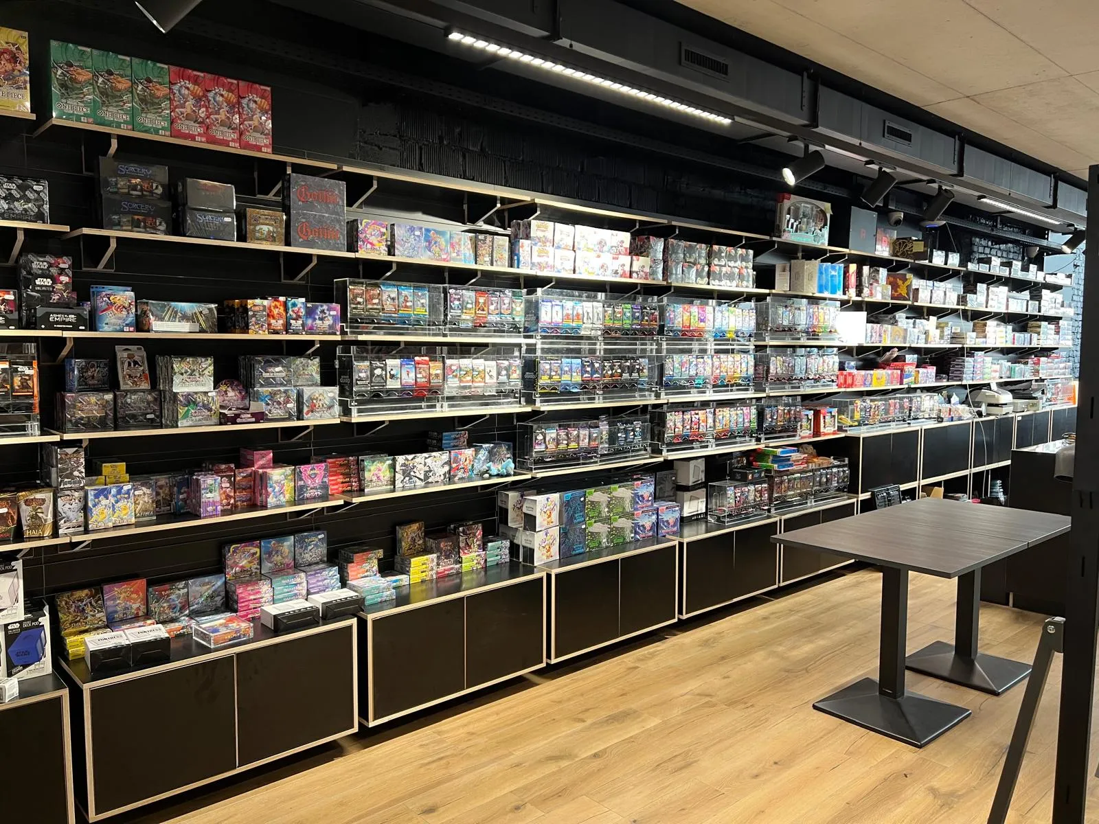 A long wall of sealed booster boxes and card products in acrylic cases