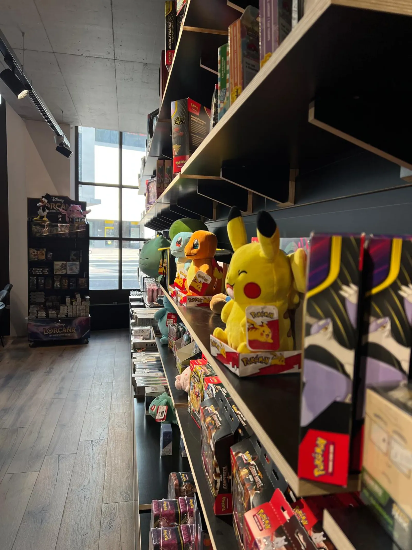 Pokémon plushies and boxes along the shelves with daylight from the shopfront