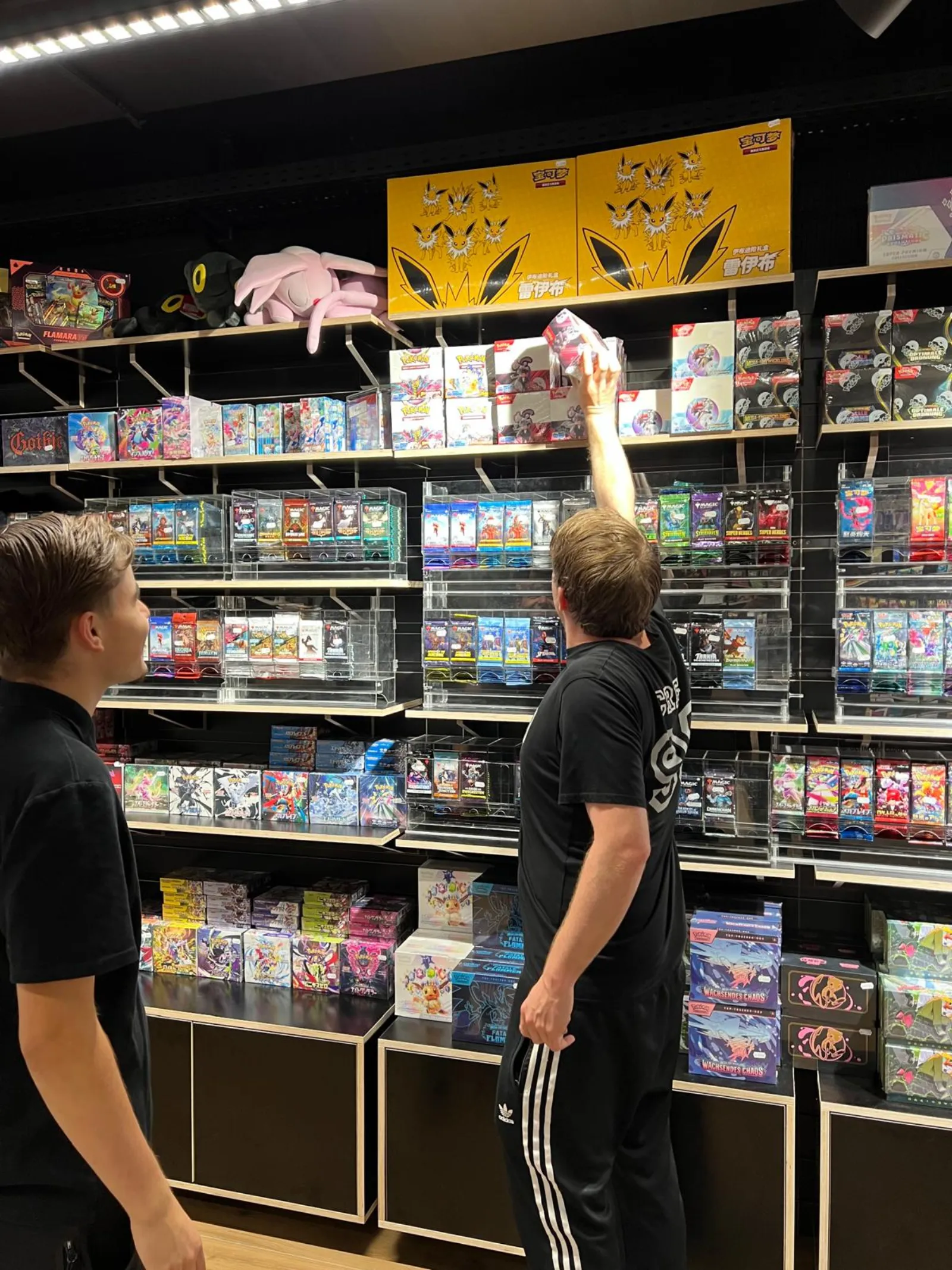 Two customers picking booster packs from the Pokémon wall